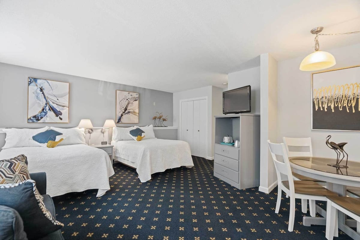 A hotel room with two beds, a desk with a chair, a TV, and artwork on the walls.