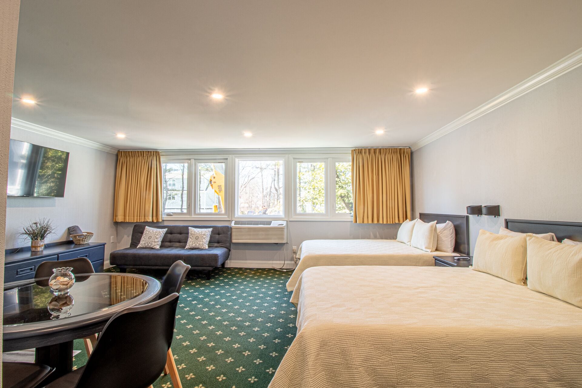 A hotel room with two beds, a sofa, a dining table, and a TV.