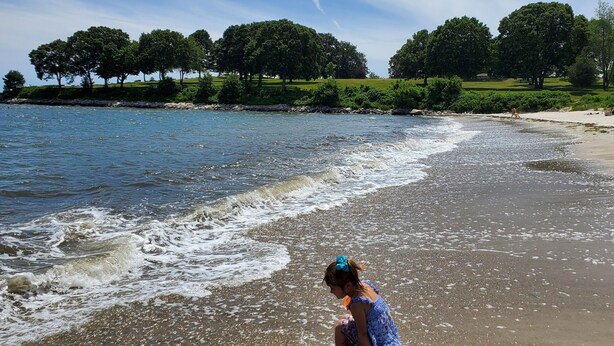 A beach scene with a child playing in the sand, trees in the background, and a rainbow in the sky. - The Niantic Inn (Niantic)