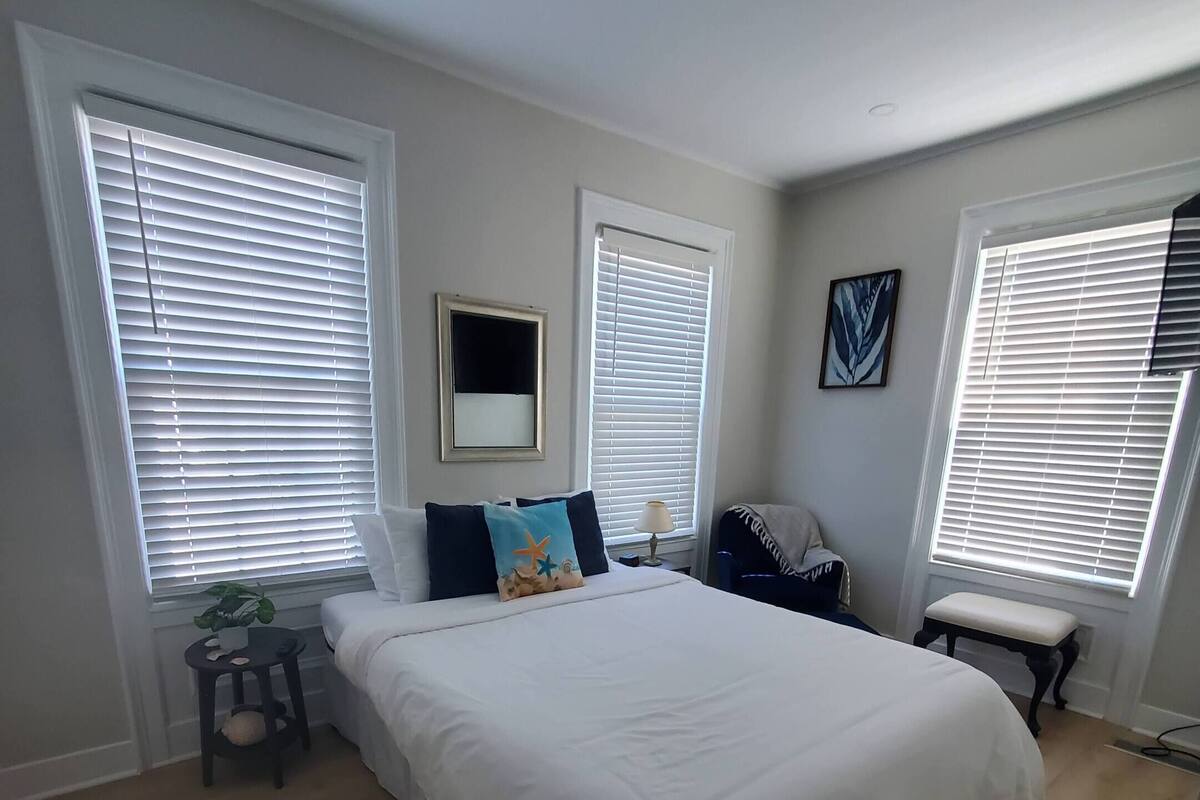 A bedroom with a large bed, a bedside table with a lamp, a bench, and a potted plant.
