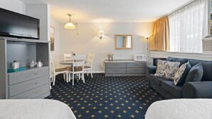 A compact hotel room with a bed, a sofa, a dining table with chairs, a small kitchen area, and a window with curtains. - The Niantic Inn (Niantic)