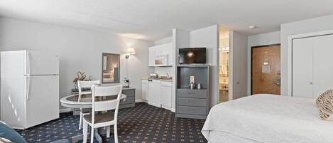 A compact hotel room with a bed, a small kitchenette, a dining area with a table and chairs, and a bathroom.