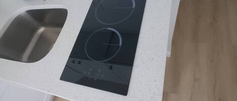 Una cocina con un lavamanos de acero inoxidable, una placa de inducción negra y una encimera blanca.