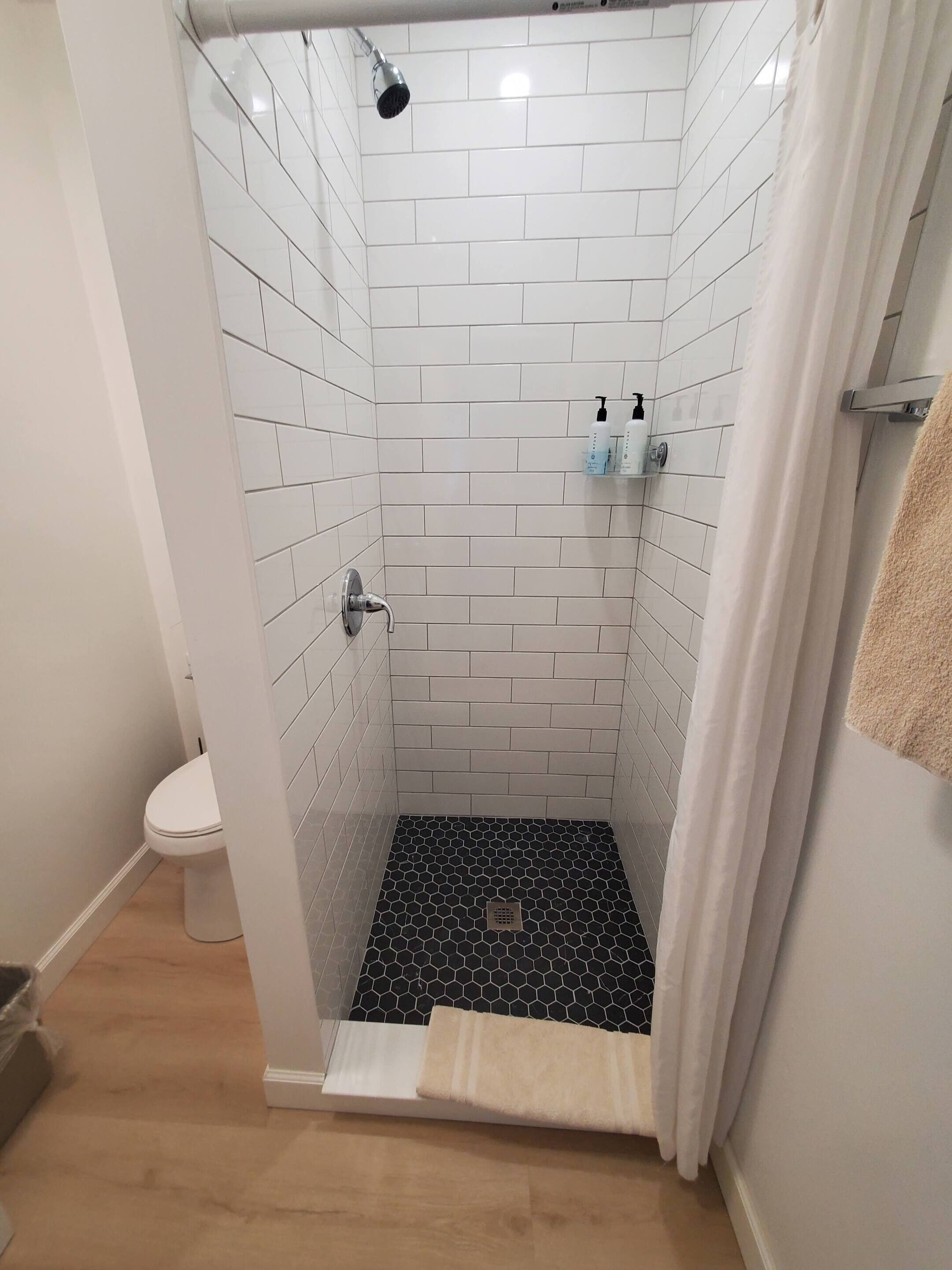 A shower with white tiles, a black hexagonal floor, and a white curtain.