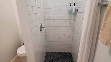 A shower with white tiles, a black hexagonal floor, and a white curtain.