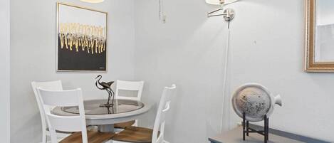 Un comedor con una mesa redonda, sillas blancas, una escultura decorativa de un pájaro e iluminación en la pared.