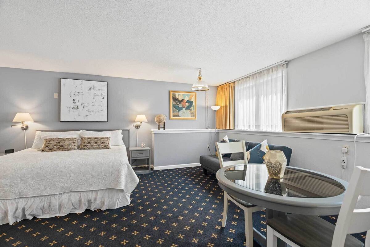 A hotel room with a bed, bedside tables, a desk, a chair, a round table, and a window with curtains.