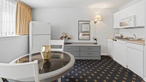 A compact hotel room with a kitchenette, a dining area with a round table, and a bed with a headboard. - The Niantic Inn (Niantic)
