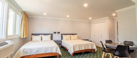 A hotel room with two beds, a desk with chairs, and a radiator.