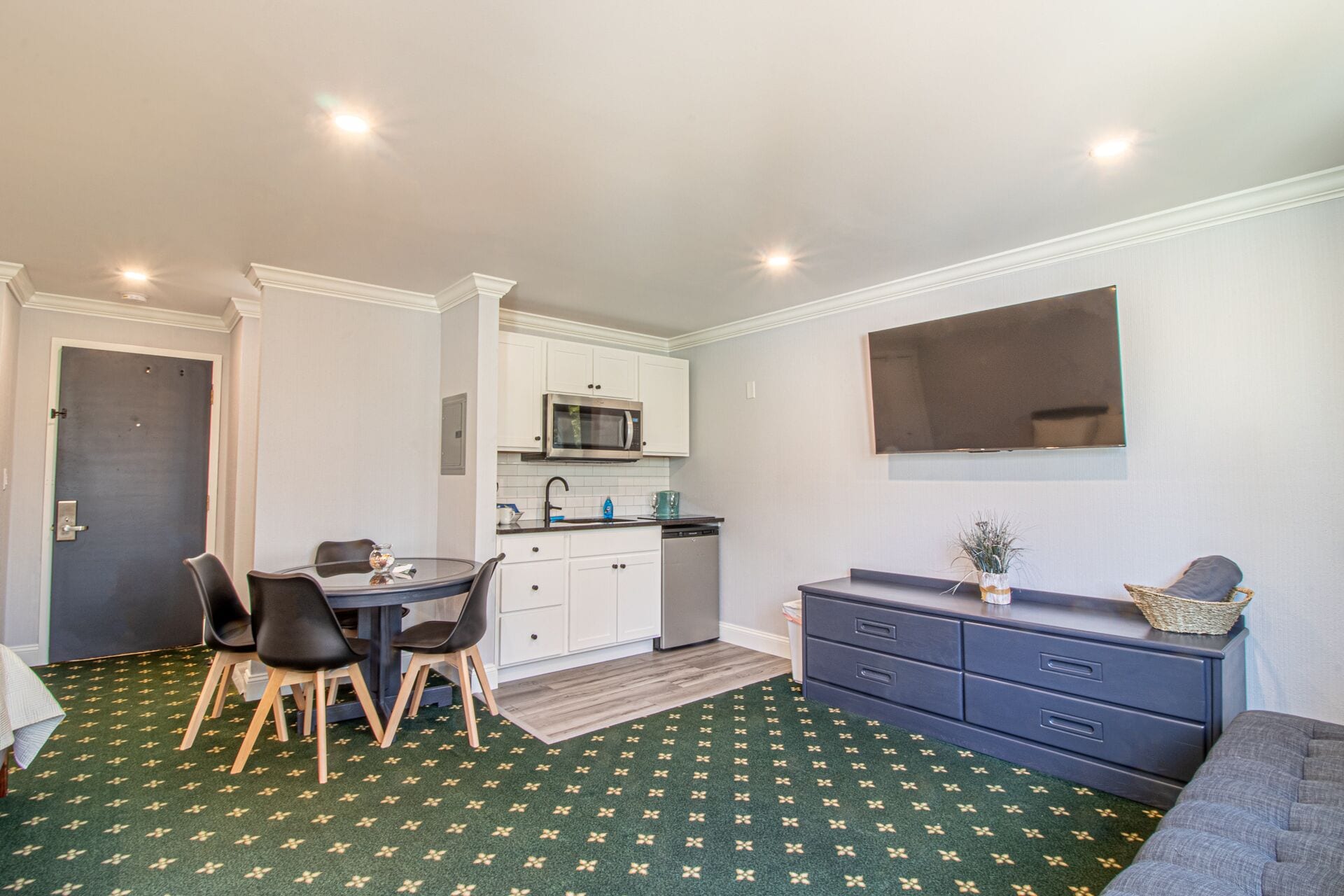 A compact kitchen with white cabinets, a microwave, and a dishwasher. There's a dining area with a table and chairs, and a grey sofa.