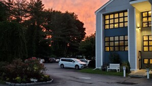 A modern building with large windows and a driveway with parked cars. - The Niantic Inn (Niantic)