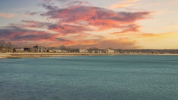 Vista para a orla marítima com paisagem urbana ao fundo durante o pôr do sol.