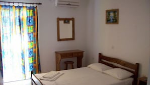 A bedroom with a bed, a wooden nightstand, a small table, a mirror, and a window with curtains. - Petros Studios (Kefalonia)