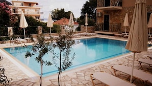 A swimming pool with lounge chairs and umbrellas, surrounded by stone tiles and a small tree. - Petros Studios (Kefalonia)