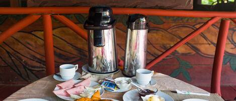 A table set with breakfast items including eggs, bread, and fruit, with a coffee maker and thermos on the table.