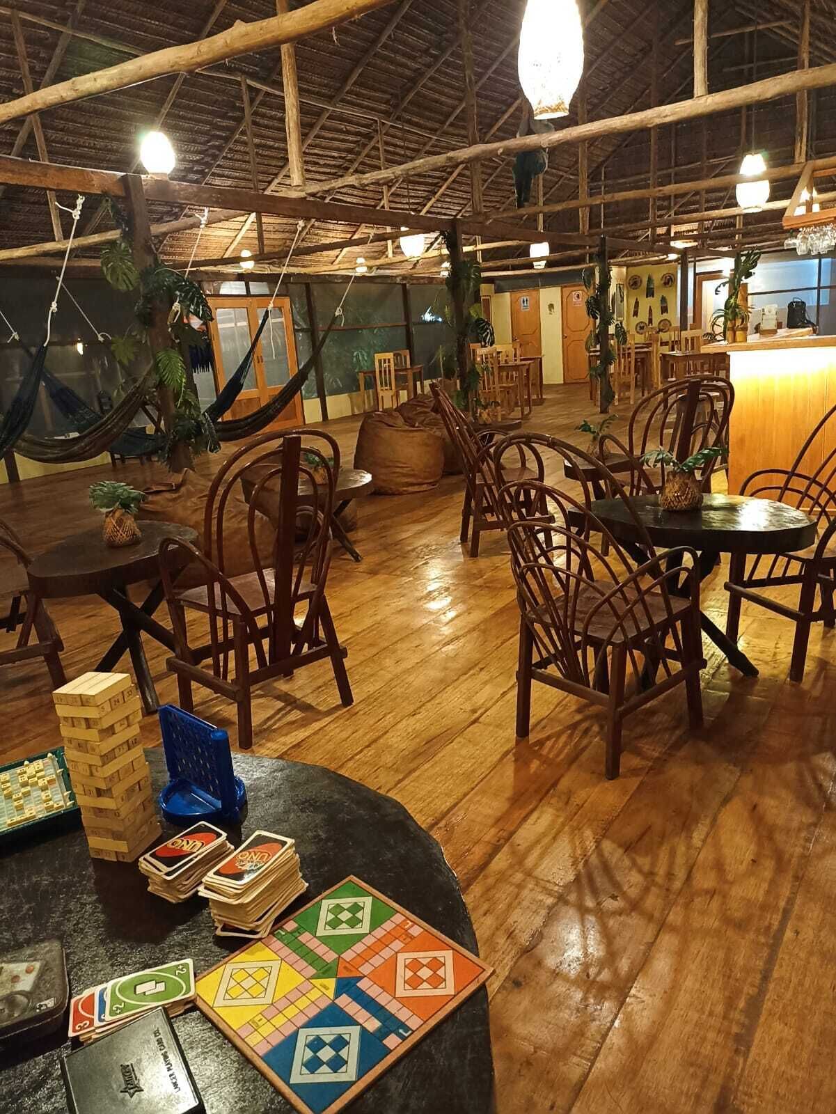 Amplio espacio interior con piso de madera, varias mesas y sillas de madera, y una variedad de juegos de mesa.