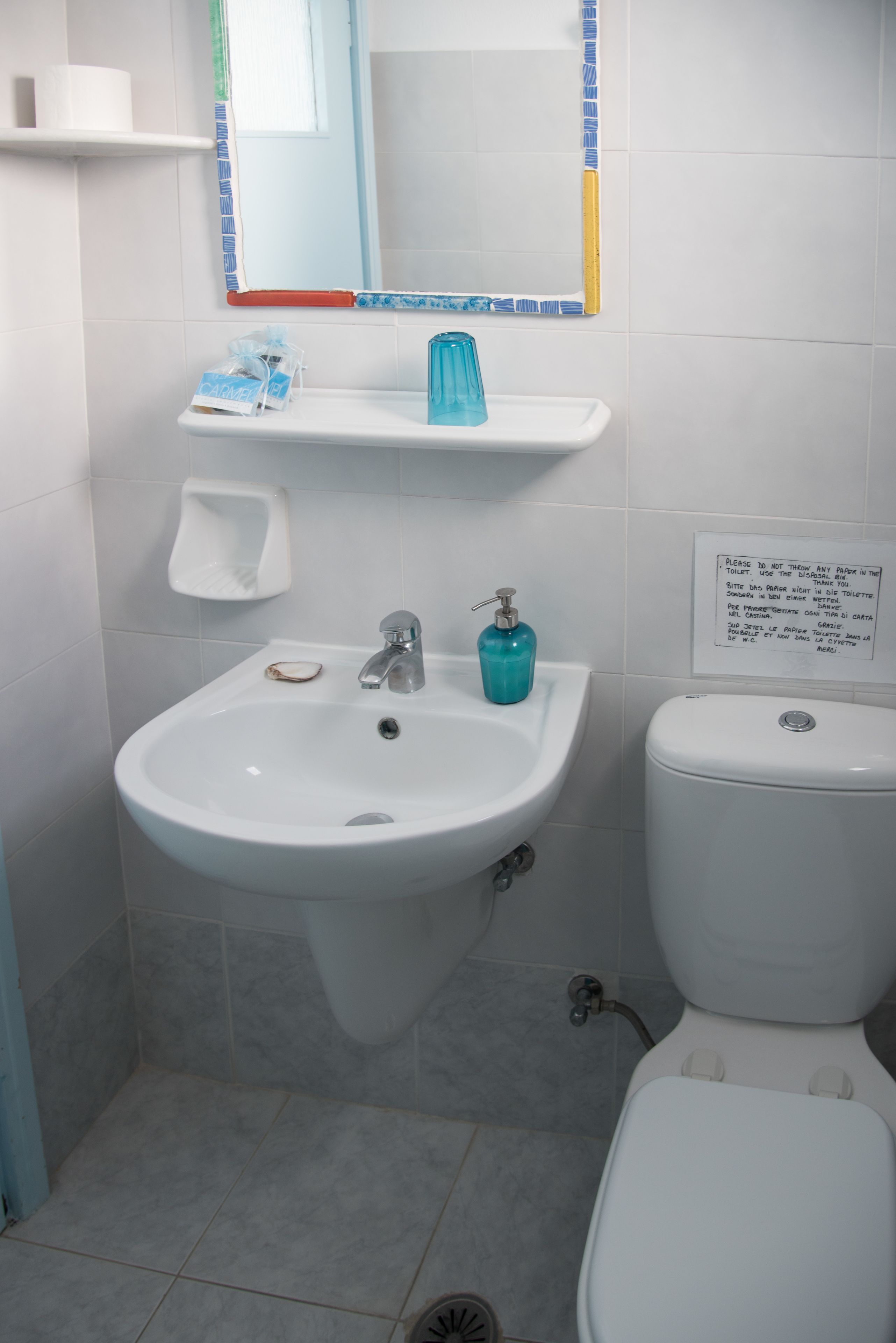 A bathroom with a white sink, a blue soap dispenser, a toilet, and a sign on the wall.