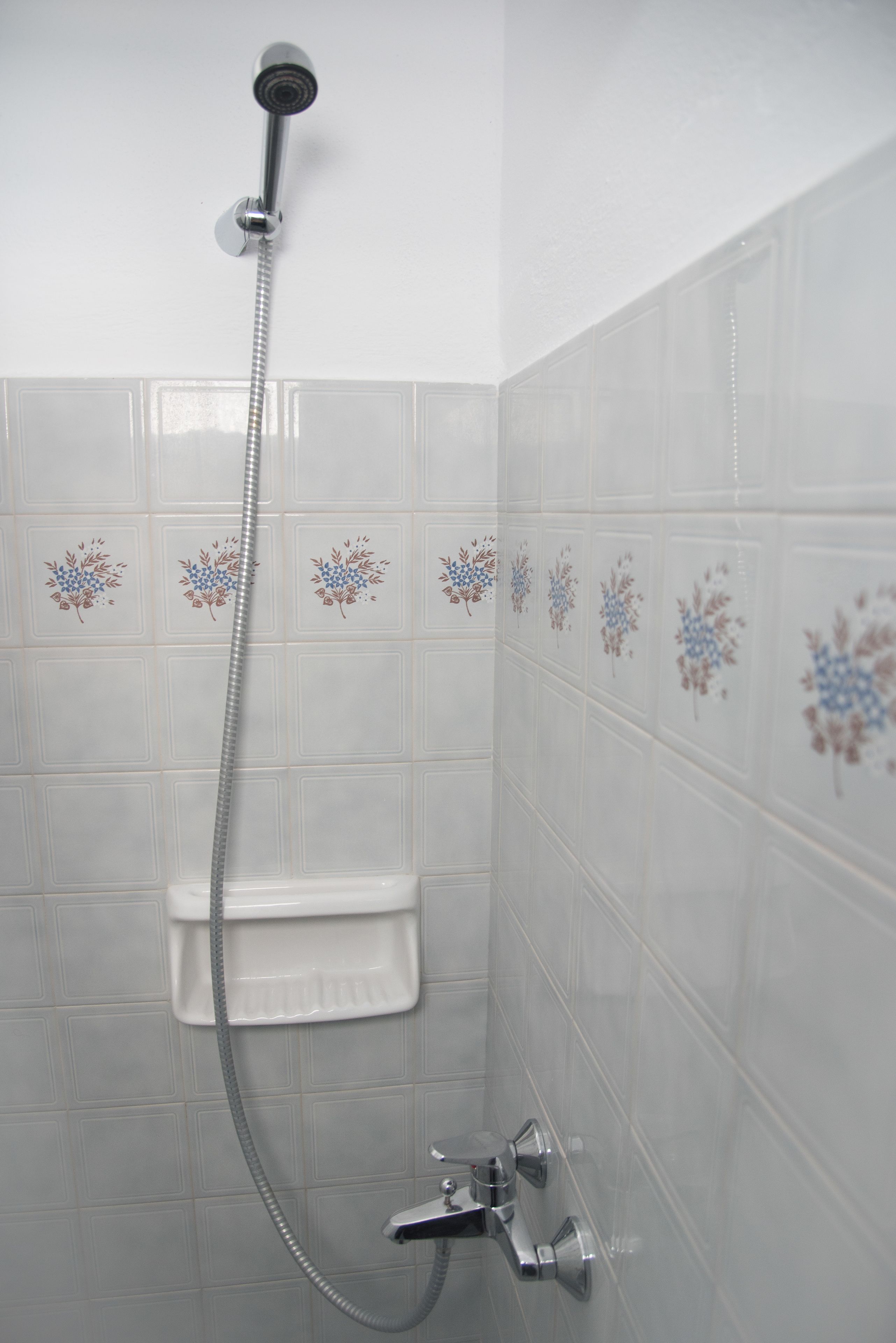 A shower with a handheld hose, a built-in seat, and decorative floral tiles on the wall.