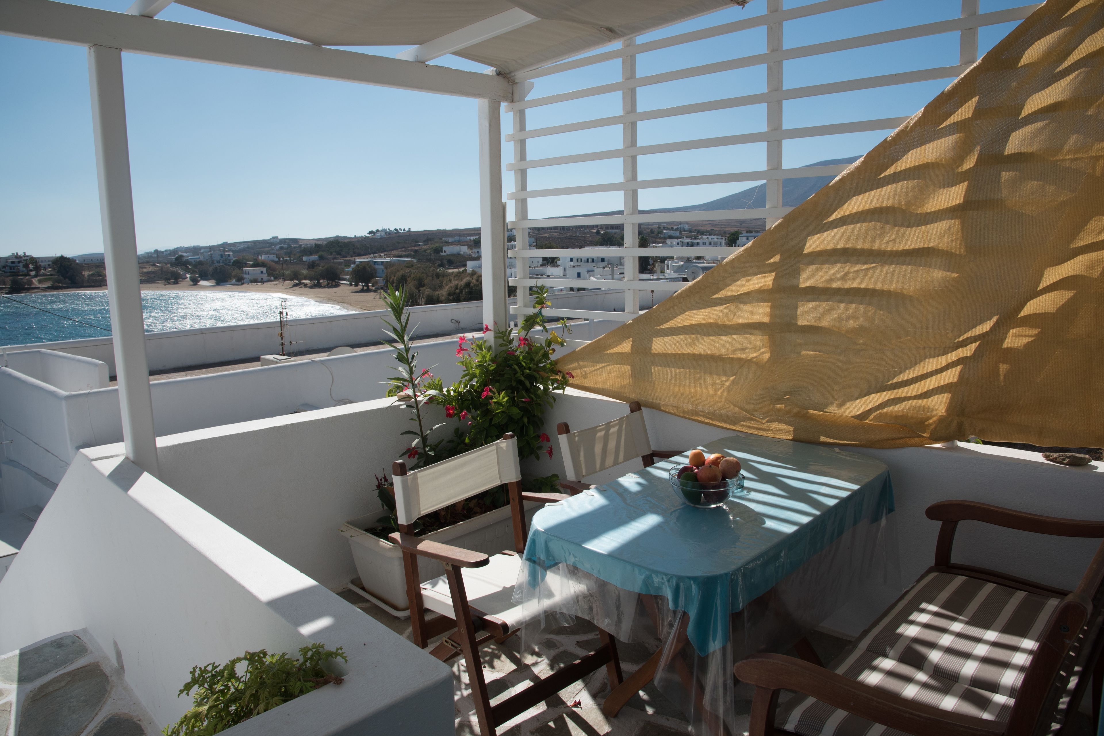 Un balcon avec une table et des chaises, offrant une vue sur la côte, avec des bâtiments et une montagne en arrière-plan.