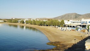 Una zona de playa costera con vista despejada al mar, una playa de arena y una hilera de edificios con una decoración blanca y azul.