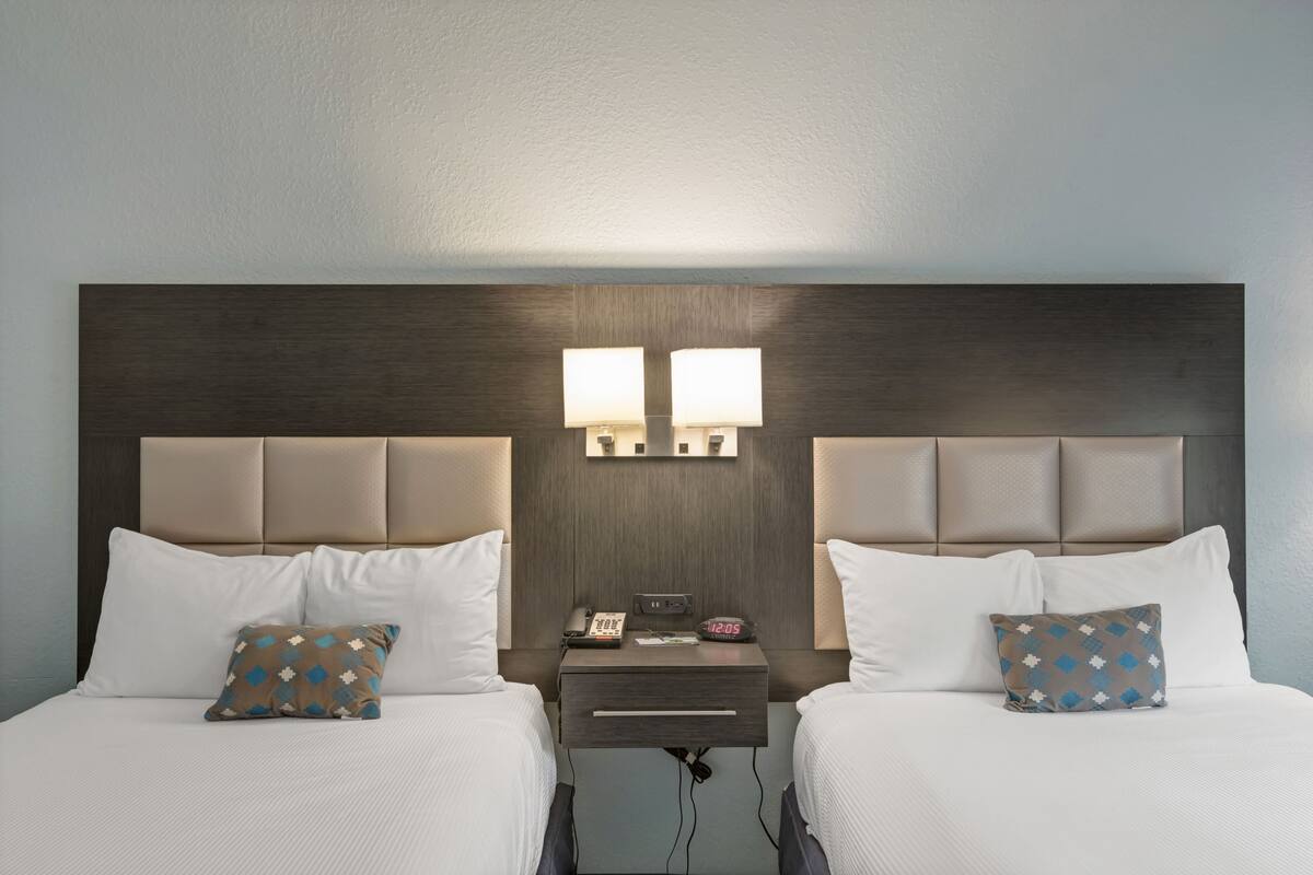 Une chambre d’hôtel avec deux lits, chacun équipé d’un oreiller, d’une table de chevet avec une lampe et d’une petite table de nuit avec un téléphone et une horloge.
