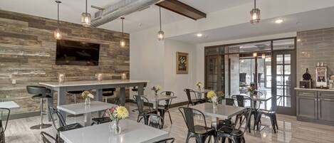 A modern dining area with multiple tables and chairs, a fireplace, and a kitchen area visible through glass doors.