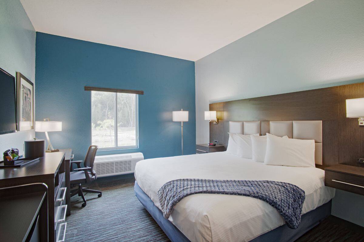 Une chambre d’hôtel avec un grand lit, un bureau avec une chaise, deux lampes de chevet et une fenêtre.