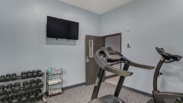 A gym with treadmills, dumbbells, and a television on the wall.