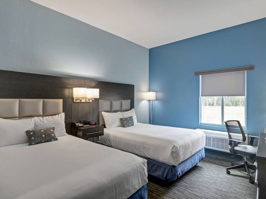 A hotel room with two beds, a desk, and a window with a view.