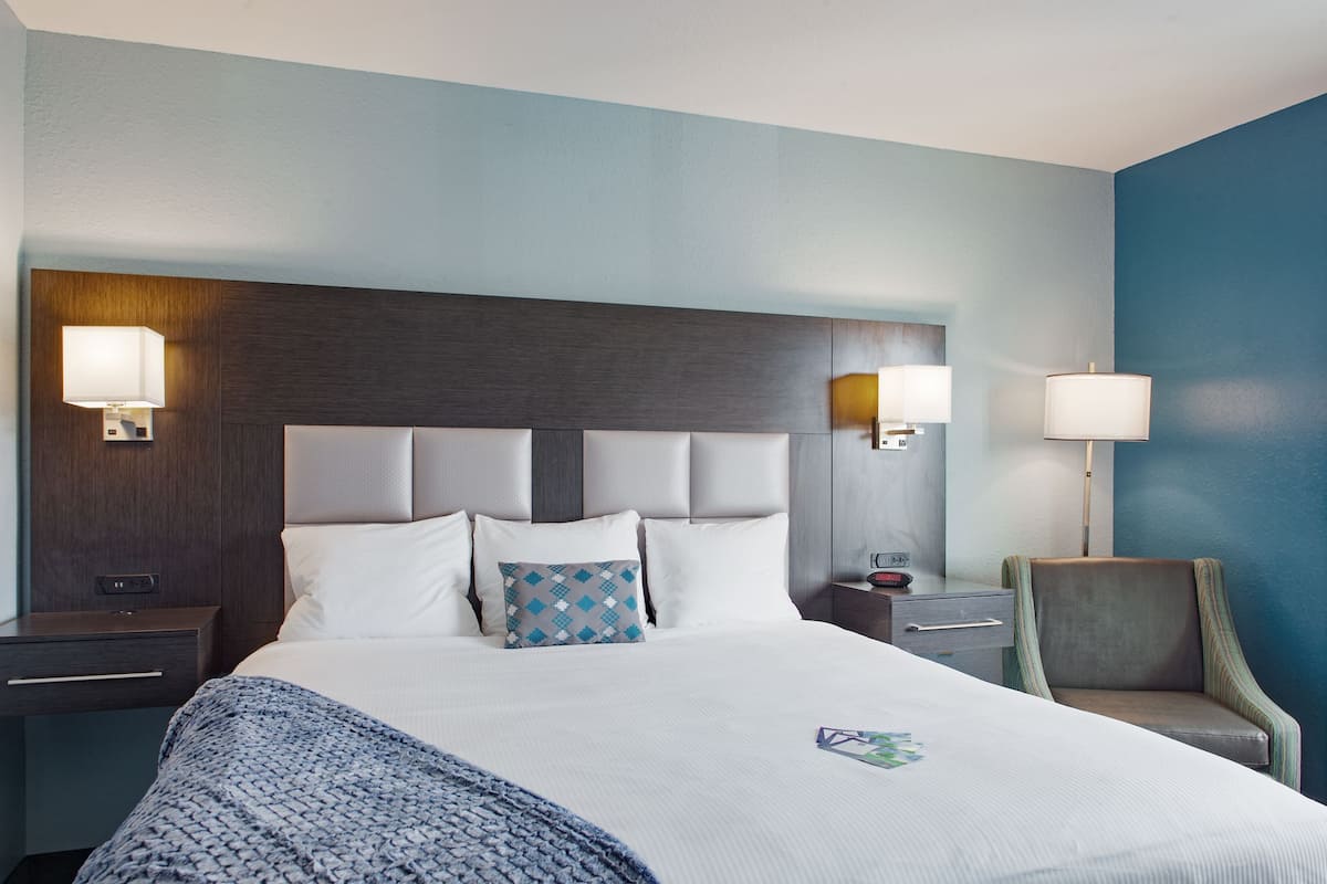 Une chambre d’hôtel avec un grand lit, deux tables de chevet, une chaise et une tête de lit agrémentée d’appliques murales.