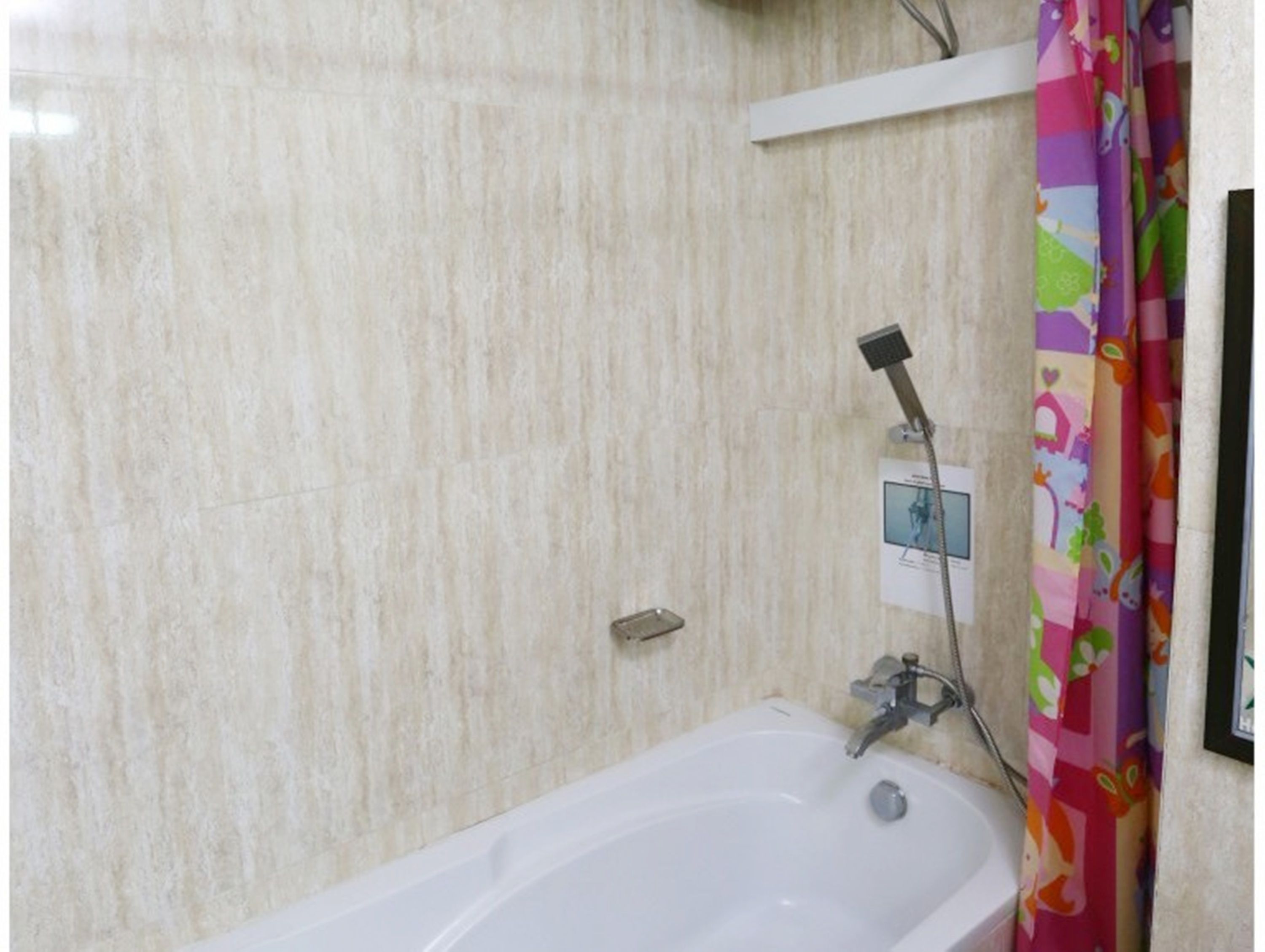 Un baño con una bañera blanca, un cabezal de ducha y una cortina colorida.