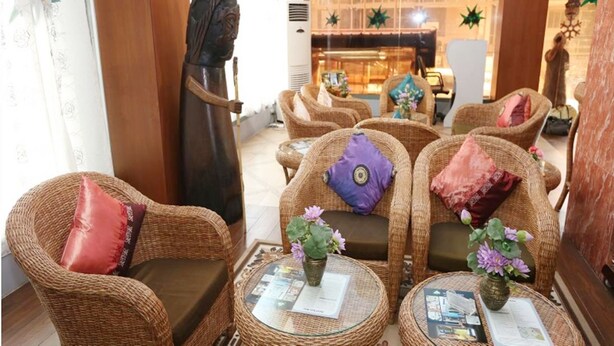 Un vestíbulo con mobiliario de mimbre, incluyendo sillones y un sofá, con cojines y una pequeña mesa con un jarrón de flores.