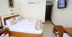 Habitación de hotel con cama, televisión montada en la pared, mesita de noche de madera y una pequeña mesa.