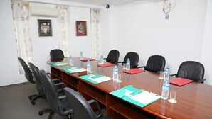 Un salón de conferencias con una larga mesa de madera, sillas negras, botellas de agua y carpetas rojas.