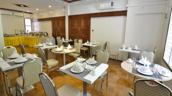A dining area with round tables and chairs, a yellow tablecloth-covered buffet in the background, and wooden paneling on the walls. - Serene Valley Hotel (Yangon)