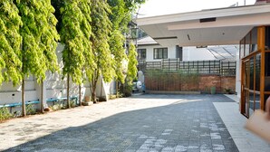 Un patio con un sendero empedrado, un árbol, un edificio con ventanas amplias y una cerca.