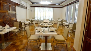 Un comedor con varias mesas y sillas, dispuesto en una habitación amplia con suelo de madera y ventanas grandes.