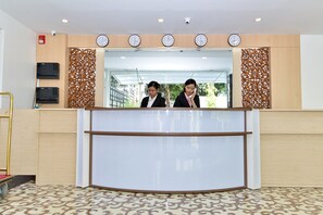 Zona de recepción con un mostrador curvo, dos recepcionistas, un reloj y una cámara de seguridad.