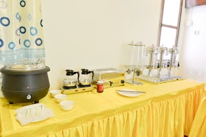 A table with a yellow tablecloth, a black pot, a coffee maker, a toaster, and several glass containers. - Serene Valley Hotel (Yangon)
