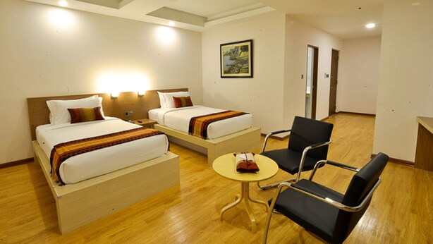Habitación de hotel con dos camas, una mesita, una silla y un cuadro en la pared.