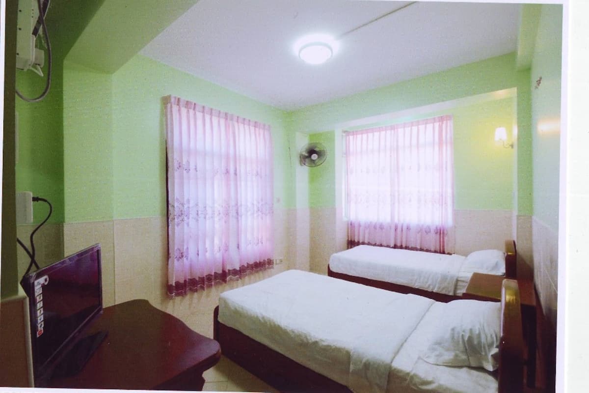Une chambre avec deux lits, un bureau et un ventilateur.