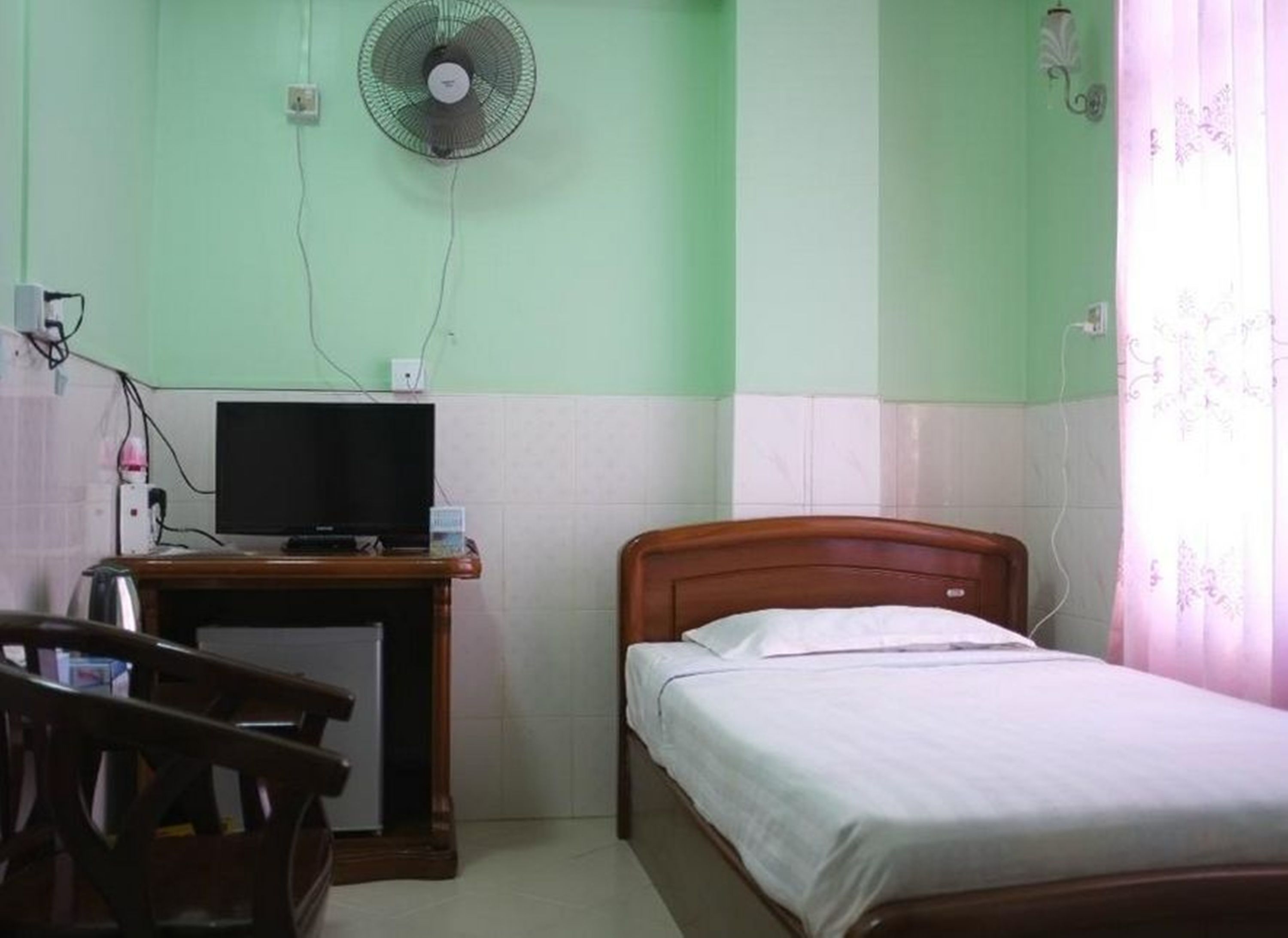 Una habitación con una cama, un escritorio con televisor, un ventilador y una silla.