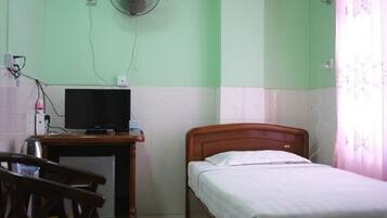 Una habitación con una cama, un escritorio con televisor, un ventilador y una silla.