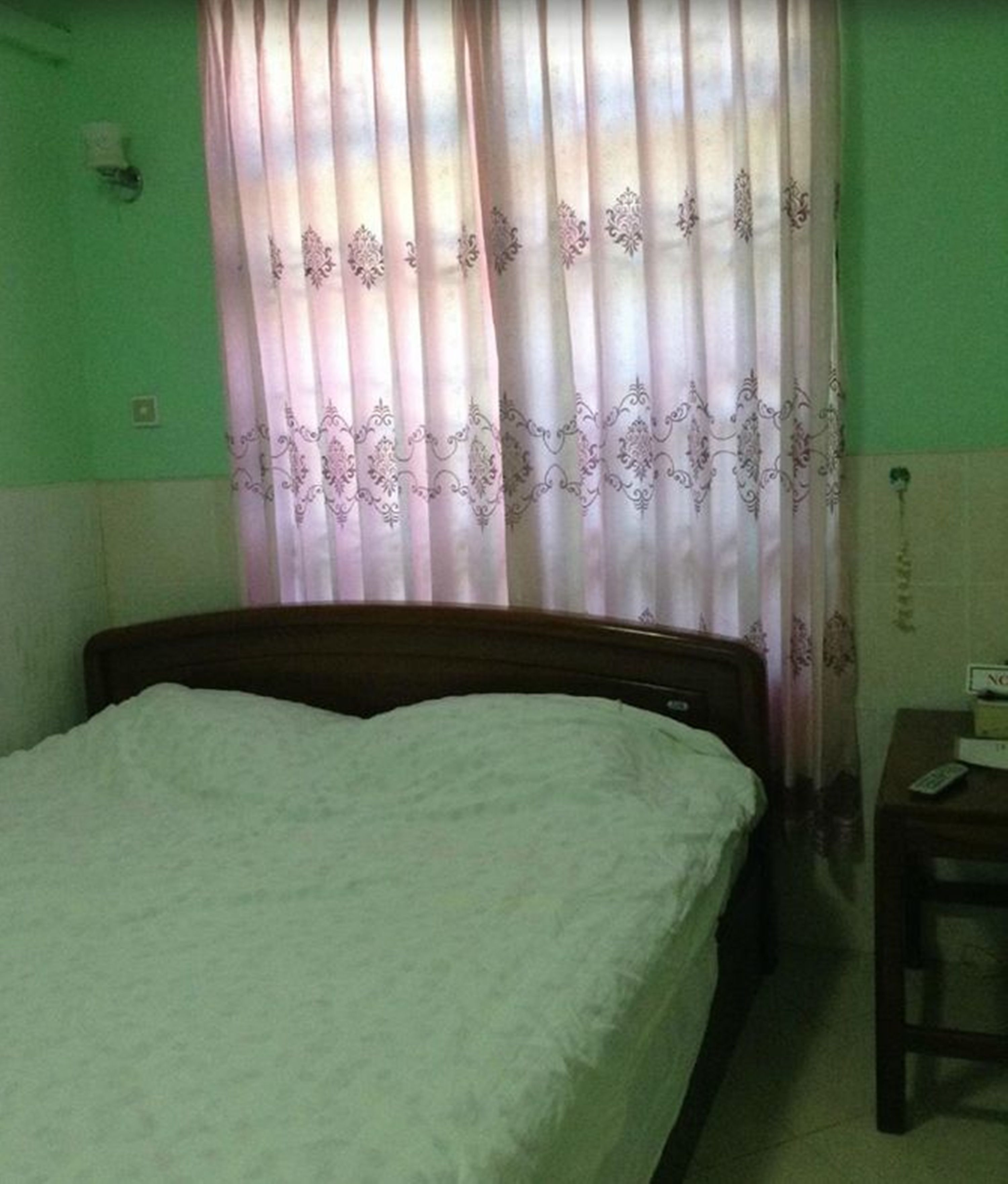 Una habitación con cama, una mesita pequeña y una cortina de estampado floral.