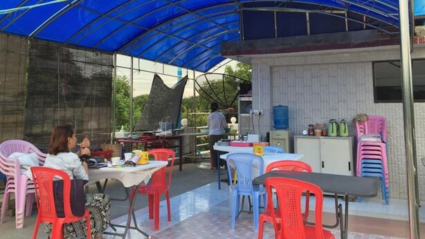 Un área de comedor al aire libre con un toldo azul, mesas, sillas y dispensador de agua.
