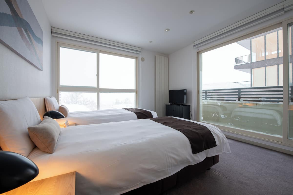 A hotel room with two beds, large windows, a balcony, and a flat-screen TV.