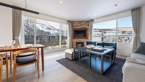 Un salon moderne doté d’une cheminée, d’un coin repas et de grandes fenêtres donnant sur un paysage enneigé.