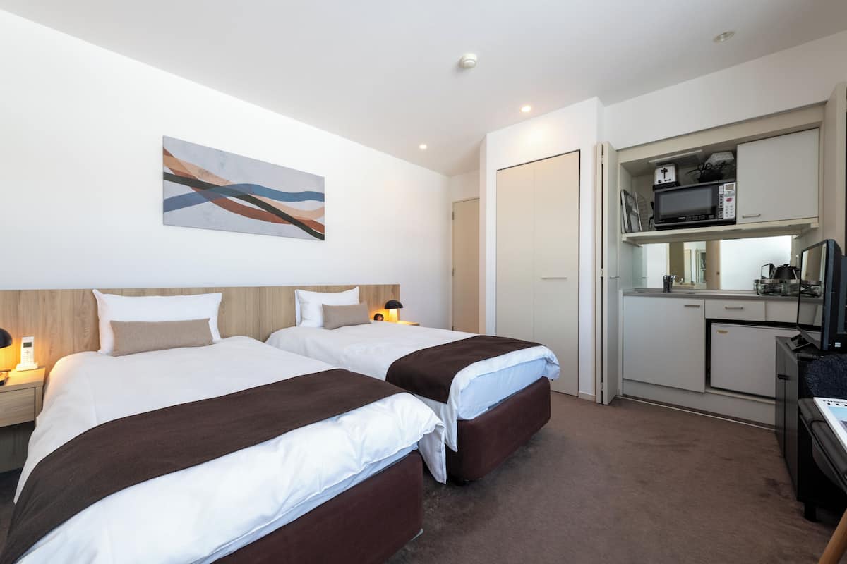 A hotel room with two beds, a kitchenette, and a painting on the wall.