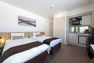Quarto de hotel com duas camas, uma cozinha compacta e um quadro na parede.
