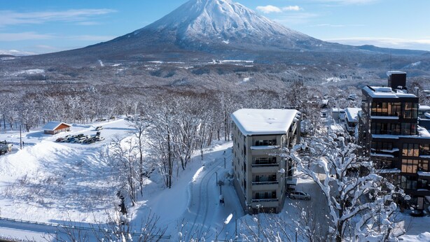 Un paysage enneigé avec une montagne imposante en arrière-plan, un bâtiment à étages et un espace de stationnement.